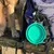 Foldable green silicone bowl attached to a blue backpack with carabiner. Suitable for travel.