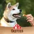 Main 8in1, TASTIES. Main tenant une friandise devant un chien portant un collier. Texte visible : 8 in 1, TASTIES.