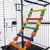 Échelle en bois multicolore suspendue à l’intérieur d’une cage métallique, avec gamelle en acier inoxydable fixée sur le côté.