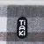 Tiaki logo on grey and brown checked fabric.