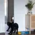 Schwarzer Hund vor einem Spiegel, daneben gelber Futternapf auf blauer Unterlage. Dekorative Vase mit Pflanzen auf Holzschrank im Hintergrund.