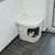 Weisse Katzentoilette mit quadratischer Öffnung, Katze sitzt innen. Geeignet für diskrete Platzierung in Ecken.