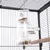 Distributeur transparent à plusieurs compartiments remplis de graines, suspendu dans une cage à oiseaux en métal avec perchoir en bois visible.