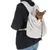 Sac de transport gris en tissu polaire porté sur le dos, avec un petit chien marron à l'intérieur. Marque TAK visible sur l'étiquette du sac.