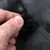 Nahaufnahme einer Hand, die einen schwarzen Klettverschluss an einem schwarzen Material öffnet.