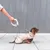 Cane con cappotto beige al guinzaglio Flexi. Una mano tiene il guinzaglio, il cane è seduto su un marciapiede davanti a una parete metallica.