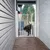 Barrière de sécurité blanche en métal installée dans un passage extérieur, avec un grand chien noir et marron passant à travers la porte ouverte tenue par une main humaine.