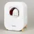 Automatic cat toilet by kooa with white design, wooden legs and controls. White cat looking out of the opening.