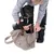 Petit chien noir et marron assis dans un sac de transport en tissu beige, une personne l’aide à s’installer. Sac avec poignées et fermeture éclair visibles.