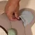 Hand legt ein Leckerli unter eine Stoffklappe auf einem Spielzeug mit grünem gepunktetem Ball und Kratzfläche.