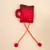 Red fabric toy in the shape of a cup with a brown top, white dots, and two yellow-red ribbons with red pom-poms.