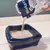 Biokat's Diamond Care cat litter is poured into a blue cat toilet. Packaging with product name and cat visible. Biokat's Diamond Care cat litter is poured into a blue cat toilet. Packaging with product name and cat visible.