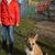 Person in a red jacket with a dog on a black and white lead outdoors. Background shows a fence and colourful graffiti.