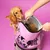 Person opening a large bag of dry pet food with kibble visible inside, while a dog stands nearby looking at the open bag.