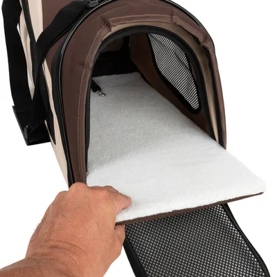Intérieur d’un sac de transport pour animaux en tissu, ouverture zippée, parois latérales avec filet, tapis amovible blanc tenu par une main visible au premier plan.