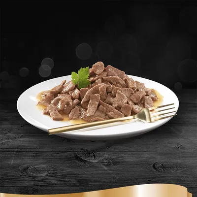 Hvid tallerken med stykker af vådfoder i sovs, pyntet med et grønt blad og en gaffel ved siden af. Ingen synlige mærker eller tekst.