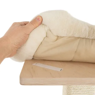 Mano levantando un cojín beige de tela suave sobre una base de madera clara, mostrando una tira de velcro visible en la superficie.