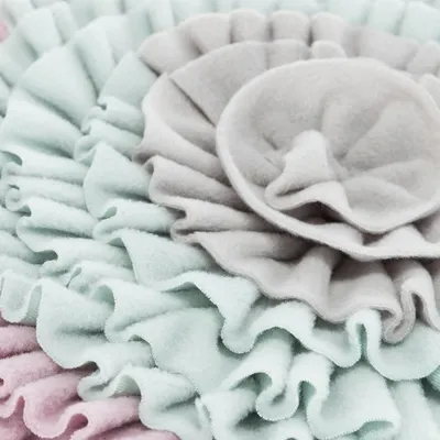 Detailní záběr na měkký filcový materiál v pastelových barvách, šedá, mátově zelená a růžová, s vrstvenou volánkovou strukturou.