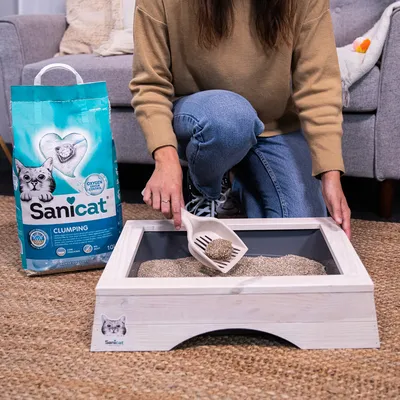 Sanicat hrudkujúca mačacia podstielka s Oxygen Control, žena čistí mačací záchod lopatkou. Balenie s mačkou a srdcom. Objem: 10 l.