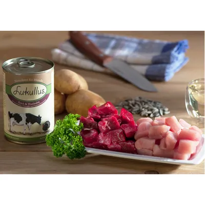 Lukullus Rind & Truthahn -koiranruokapurkki, vieressä perunoita, auringonkukansiemeniä, lasi öljyä sekä lautasella naudan- ja kalkkunanlihapaloja ja persiljaa. Tuotenimi näkyvissä.