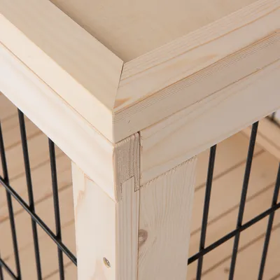 Détail d’un angle de cage pour animaux en bois clair avec barreaux métalliques noirs, assemblage visible du cadre et des panneaux en bois.