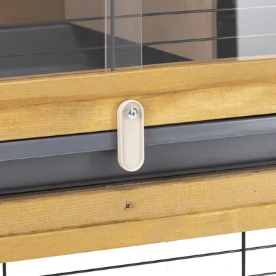 Detailný pohľad na uzatvárací mechanizmus z dreva, plastu a kovu na ohrade s plexisklom a mriežkovými prvkami.