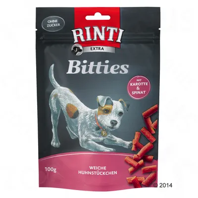 Опаковка Rinti Extra Bitties, 100 г, с надписи: Ohne Zucker, Mit Karotte & Spinat, Weiche Huhnstückchen. Изобразени са куче и парченца лакомства.