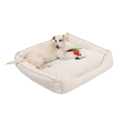 Hund liegt auf einem cremefarbenen Hundebett aus geripptem Stoff, daneben zwei bunte Spielzeuge.
