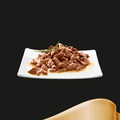 Chunks of meat in gravy served on a white square plate, garnished with green herbs, shown to illustrate the product's appearance and texture.