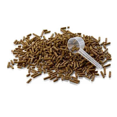 Granulki karmy w formie brązowych pałeczek, rozsypane na białym tle, obok przezroczysta plastikowa miarka.