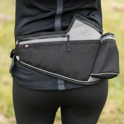 Schwarze und graue Hüfttasche mit Netzmaterial, Reissverschlüssen und Flaschenhalter, getragen um die Taille. Marke Trixie sichtbar auf der Tasche.