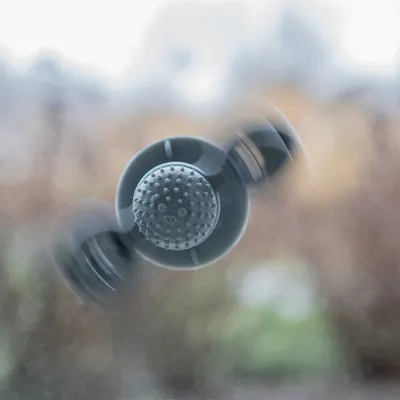 Šedá plastová hračka s přísavkou na skle, uprostřed kulatý povrch s gumovými výstupky.