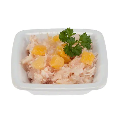 Porcja mokrej karmy w białej miseczce, widoczne kawałki mięsa, żółte kostki oraz gałązka natki pietruszki na wierzchu.