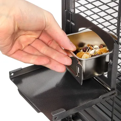 Contenitore in metallo con mangime per uccelli inserito da una mano all’interno di una gabbia nera a griglia.