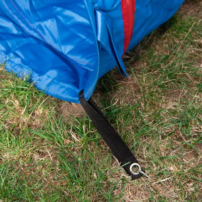 Detalj av blått tygmaterial med svart rem och metallögla, placerad på gräs. Ingen synlig varumärkes- eller produkttext.