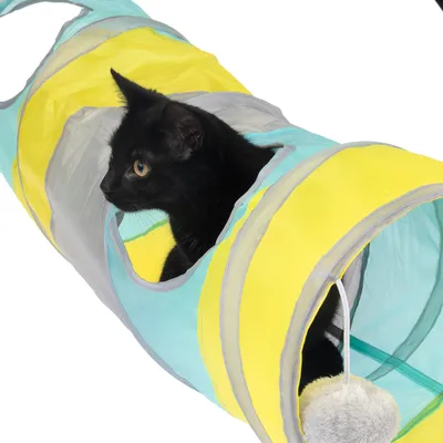 Spielzeug-Tunnel aus gelbem und blauem Stoff mit grauen Akzenten, schwarzer Katze im Tunnel und hängendem Plüschball.