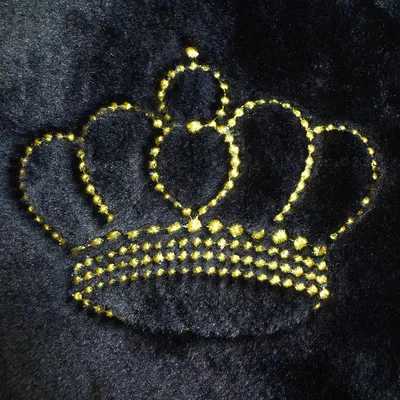 Czarna tkanina z wyszytym żółtym konturem korony, widoczna faktura materiału i haftu.