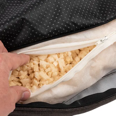Nahaufnahme eines geöffneten Kissens mit Reissverschluss, das eine Füllung aus Schaumstoffstücken zeigt.