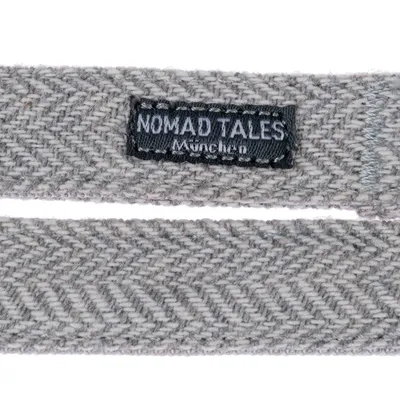 Nomad Tales München. Detailansicht eines grauen Stoffbands mit Fischgrätenmuster und Markenetikett.