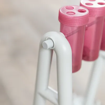 Detailaufnahme eines weissen Gestells mit rosa Kunststoffbehältern, geeignet für interaktives Spielzeug oder Futterspender.