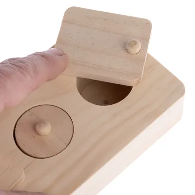 Juguete de madera con tapa deslizante que descubre una abertura redonda. Mano muestra el uso de la tapa.