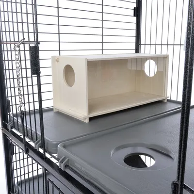 Caja de madera con dos aberturas redondas, colocada en una jaula metálica con bandejas de plástico gris y paredes de rejilla.