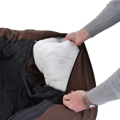 Närbild på en person som öppnar dragkedjan på en brun hundbädd och visar den vita innerkudden av tygmaterial.