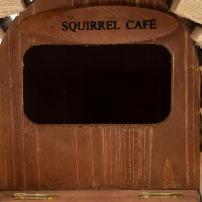 Drevená štruktúra s nápisom 'Squirrel Café' nad obdĺžnikovým otvorom. Vhodné pre veveričky alebo malé zvieratá.