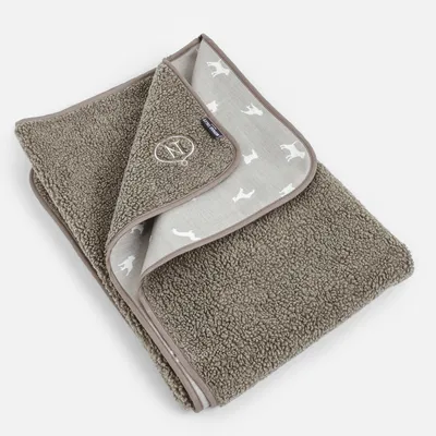 Couverture en tissu bouclette marron, bordure beige, motif silhouettes de chiens blancs sur l’envers, étiquette Soft Blanket et broderie cercle avec os visible.
