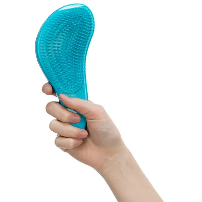 Ruka drží modrý kartáč s flexibilními štětinami, vhodný pro péči o srst.