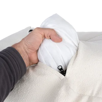Una mano muestra cómo sacar un cojín interior blanco de una funda color crema con cremallera.