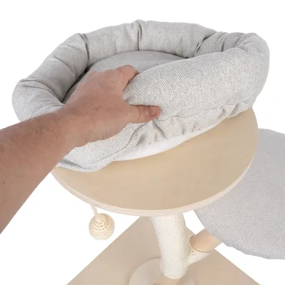 Mano muestra un cojín extraíble y acolchado sobre una plataforma redonda de madera de un árbol rascador con poste de sisal y pelota de juego.