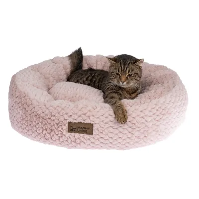 Chat allongé dans un panier rond en tissu rose, étiquette visible avec la marque Modern Living sur le devant du panier.
