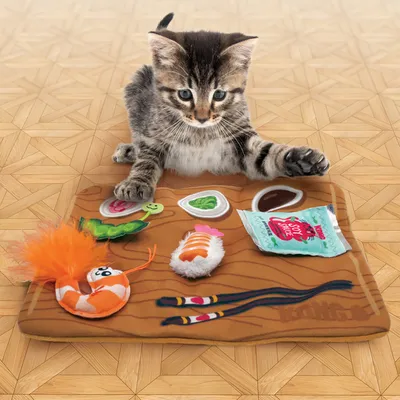 Котёнок играет с игровой подстилкой с игрушками-суши и цветными тканевыми элементами.